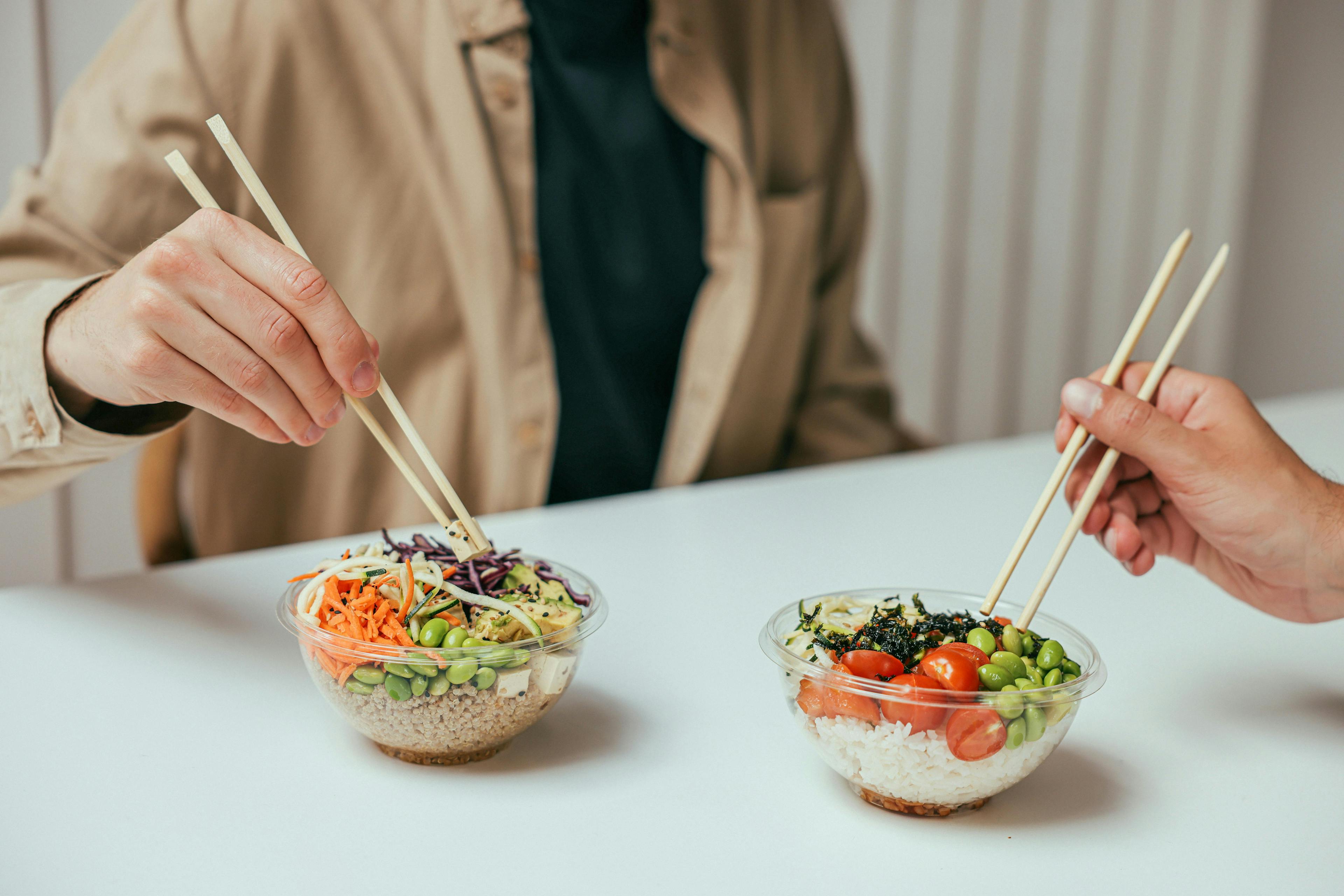 Two people eating poke bowls with chop sticks