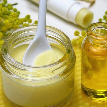 A jar of zero waste shea butter lotion with a spoon in it besides another jar of oil.