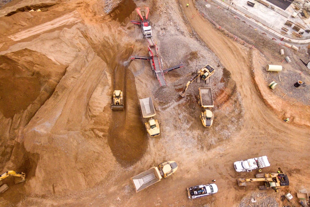 Mining site shown from above, showing machinery and vehicles over brown sandy soil.