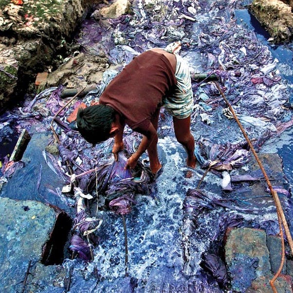 A boy standing in a polluted river caused by the production of fast fashion. Sustainable fashion doe not create such environmental problems.