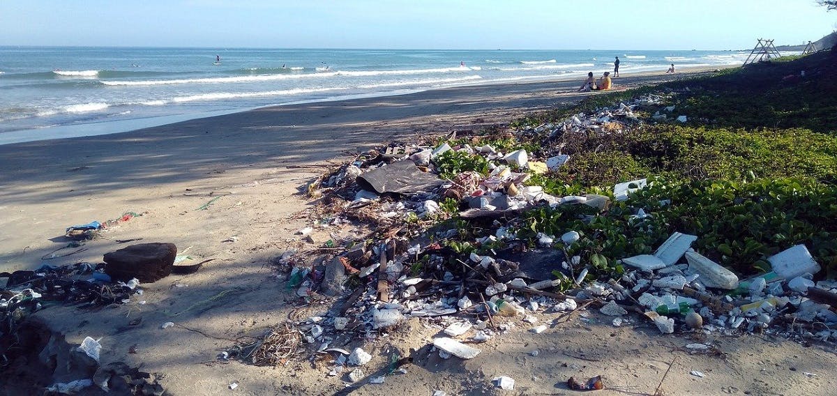 A beach polluted with waste while beach-goers go about their day.
