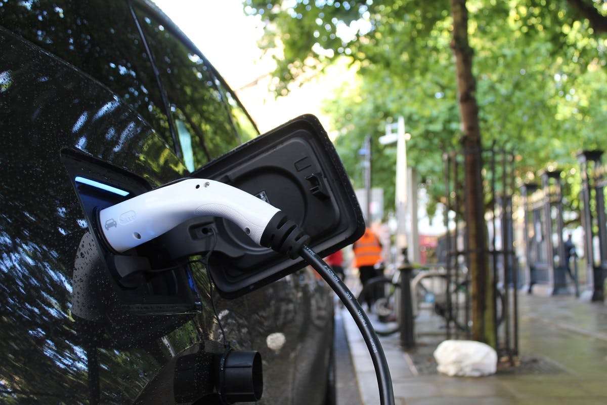 An electric car charging by the side of an urban street. Convenience of charging vs infrastructure of charging is just one of the many electric cars pros and cons debate.
