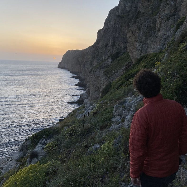 A beautiful sunset looks over a jagged coastline where land meets the sea. 