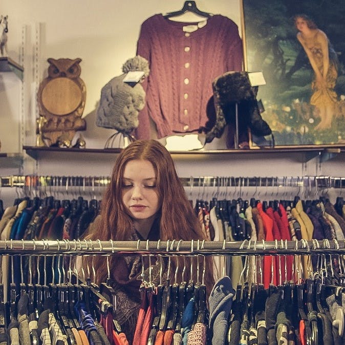 A girl browsing for clothing in a second hand shop. Shun fast fashion by purchasing second hand garments.