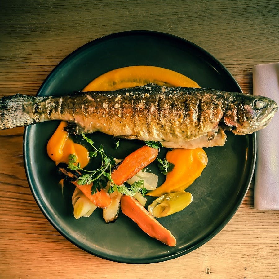 A grilled fish and colourful fresh vegetables served on a black plate