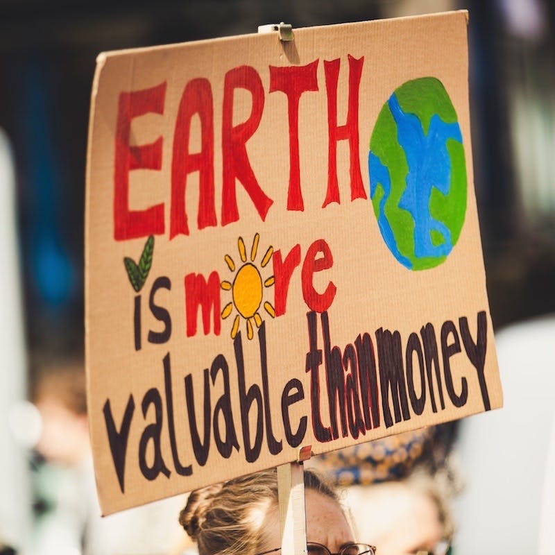 A protest sign is held up, which says: "Earth is more valuable than money".