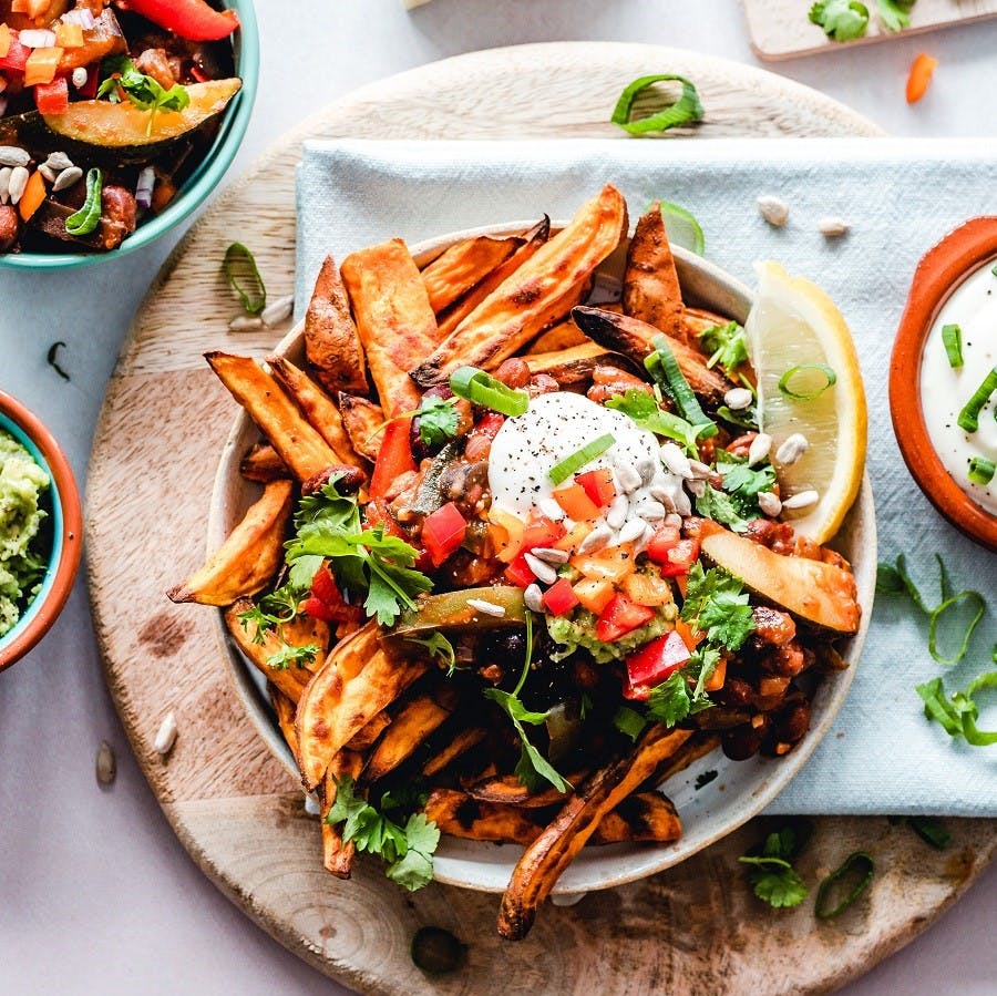 Going vegan means getting creative! A plate of sweet potato chips topped with vegan sour cream and accompanied with a side dish of guacamole