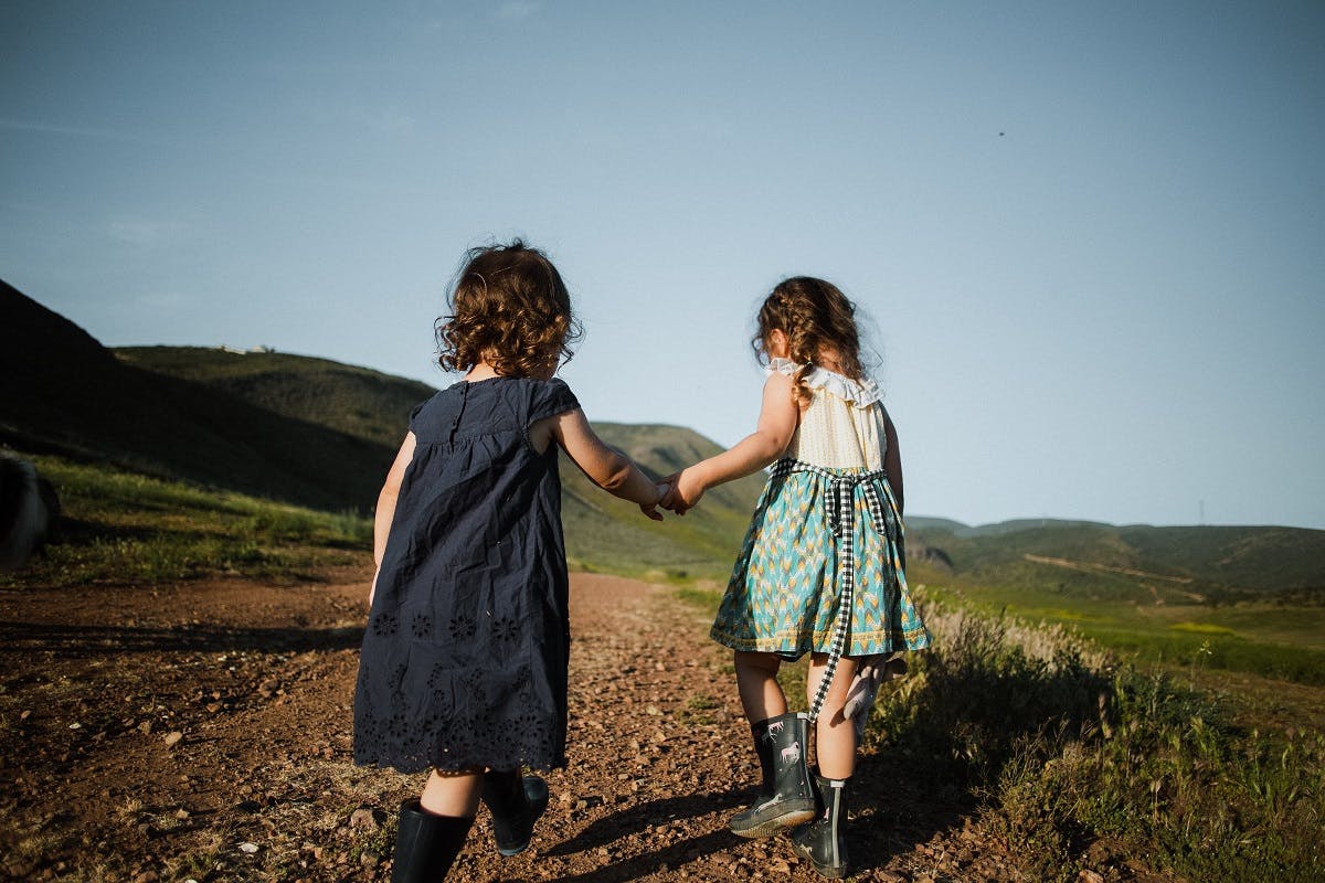Two children holding hands walking down a path in nature.