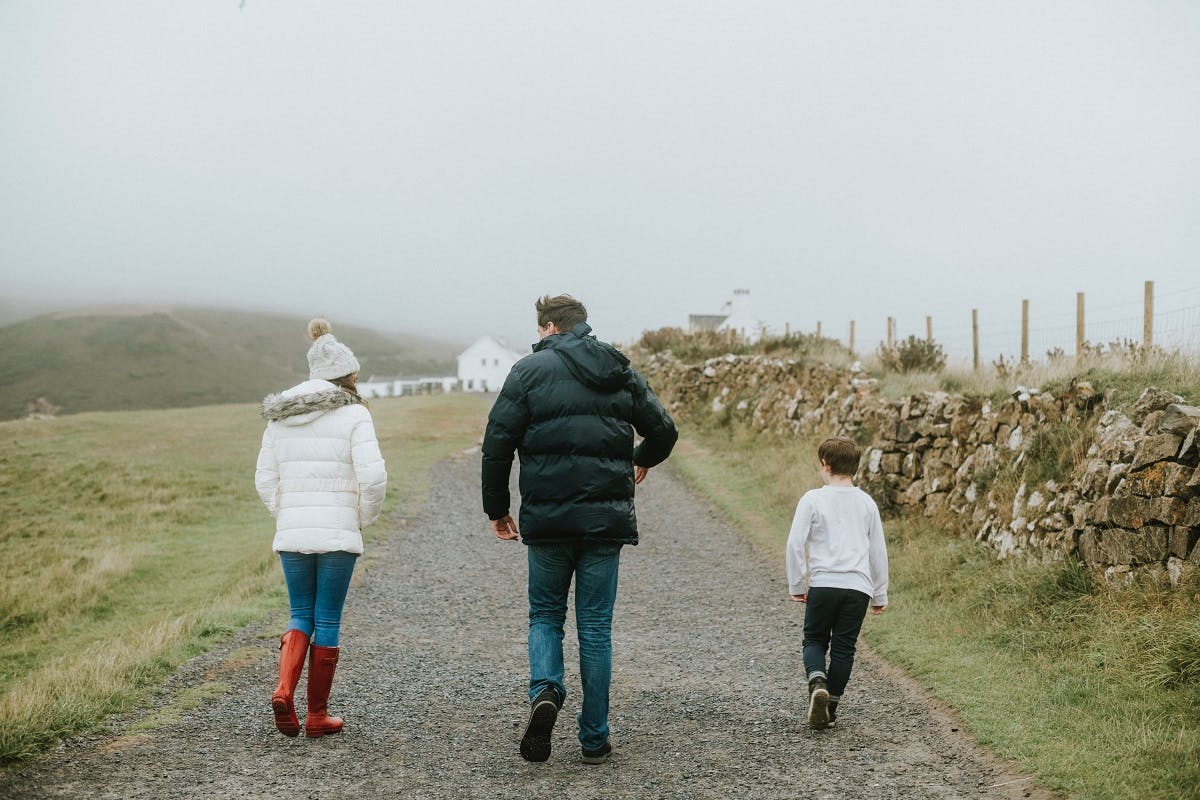 A father walks with his two children through some farmland on a misty day.