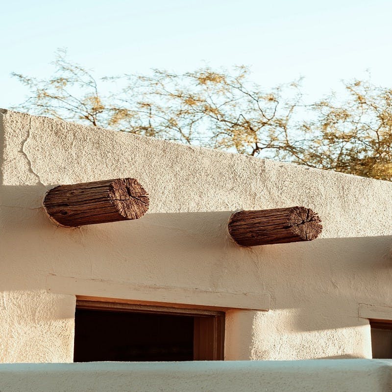 The corner of a cob house with trees in the background. Cob is a perfect material for an eco home as it is formed from materials nature has to offer.