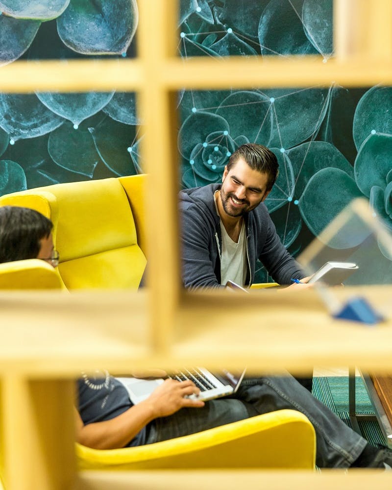 Two office workers happily chat on yellow office sofas.