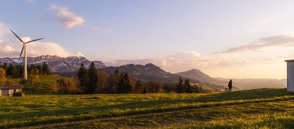 A panorama view of mountains, forest, fields and a green energy wind turbine