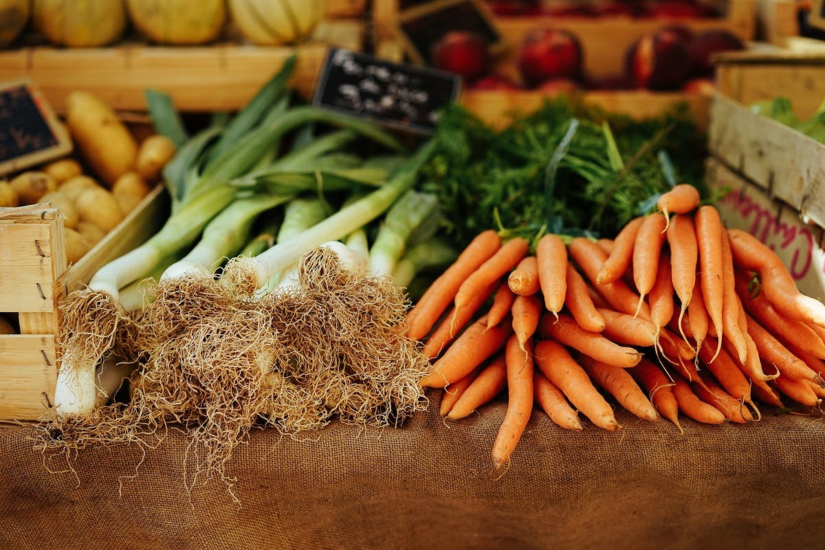 Organic leaks and carrots on sale at a farmers' market. To eat seasonally and locally helps your local farmer.