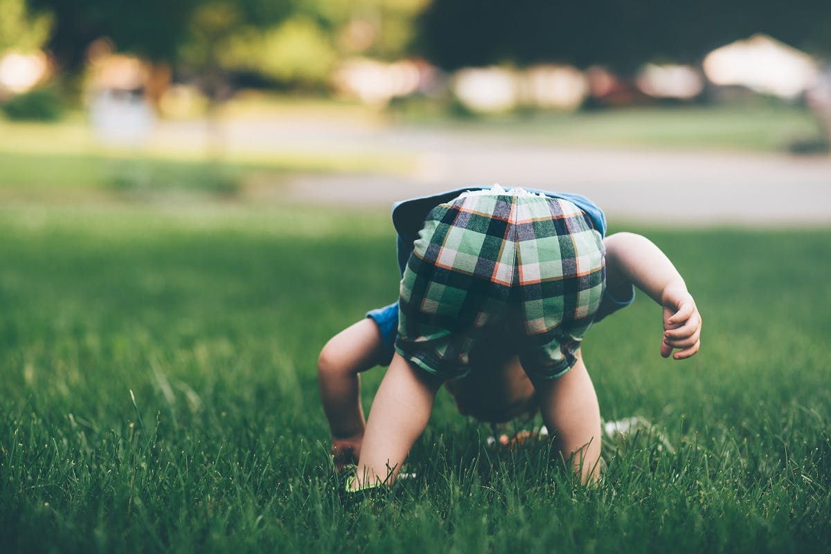 A toddler playing in the grass outside. Regular time in nature is a must when raising an eco baby.