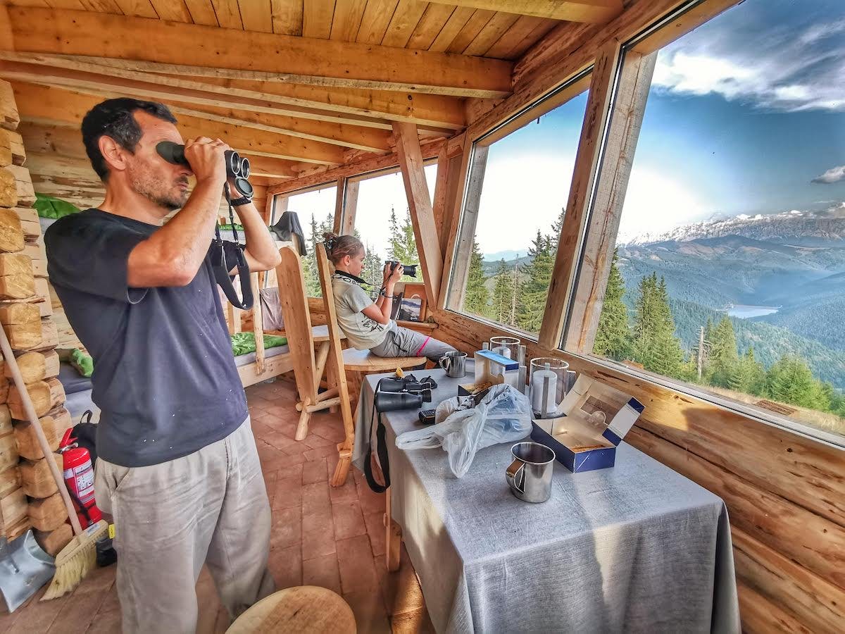 Tourists inside a wildlife hide look through binoculars and cameras