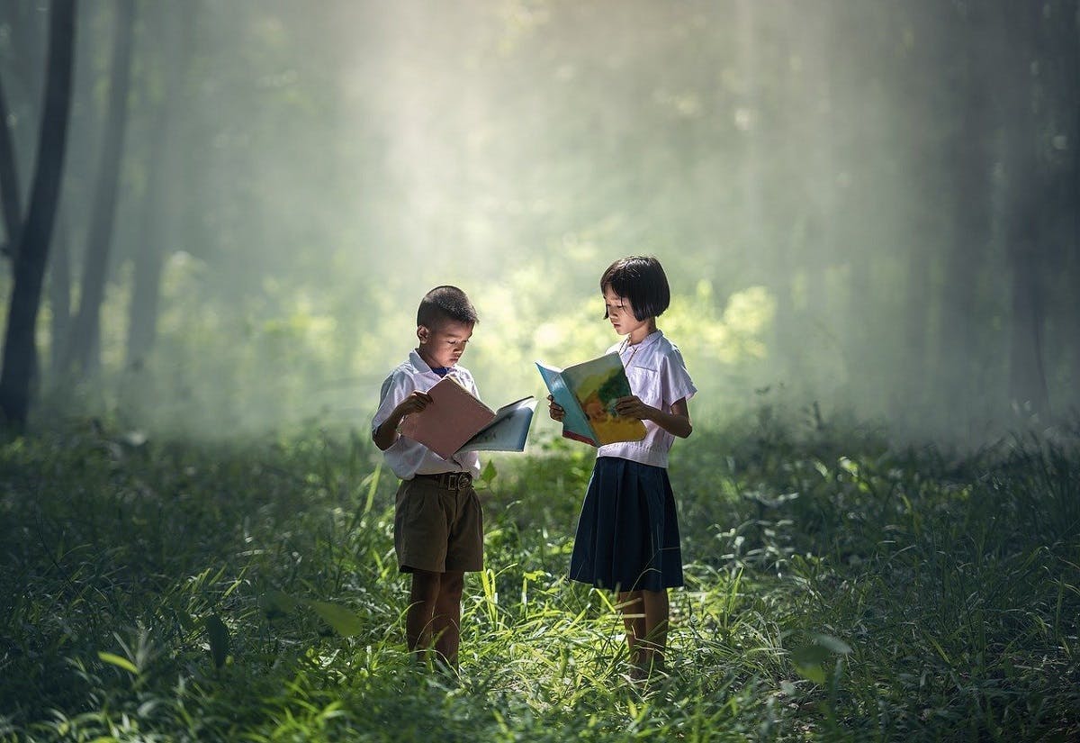 Two children reading books in a forest.