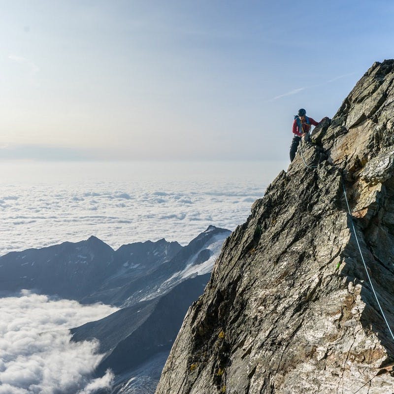 Upon a mountain above the clouds, a rock climber is seen. 
