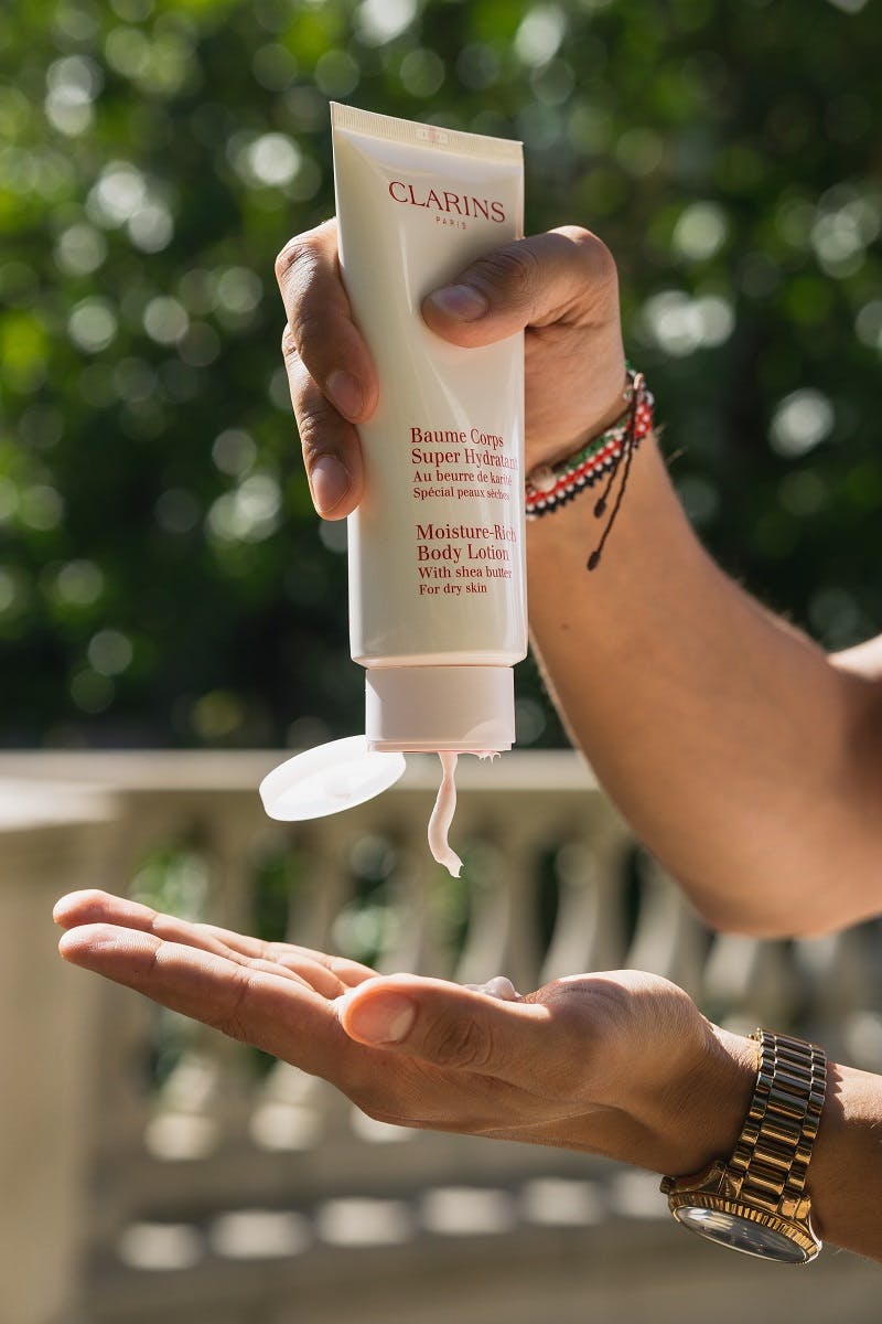 A person squeezing a tube of fragrance lotion into one hand.