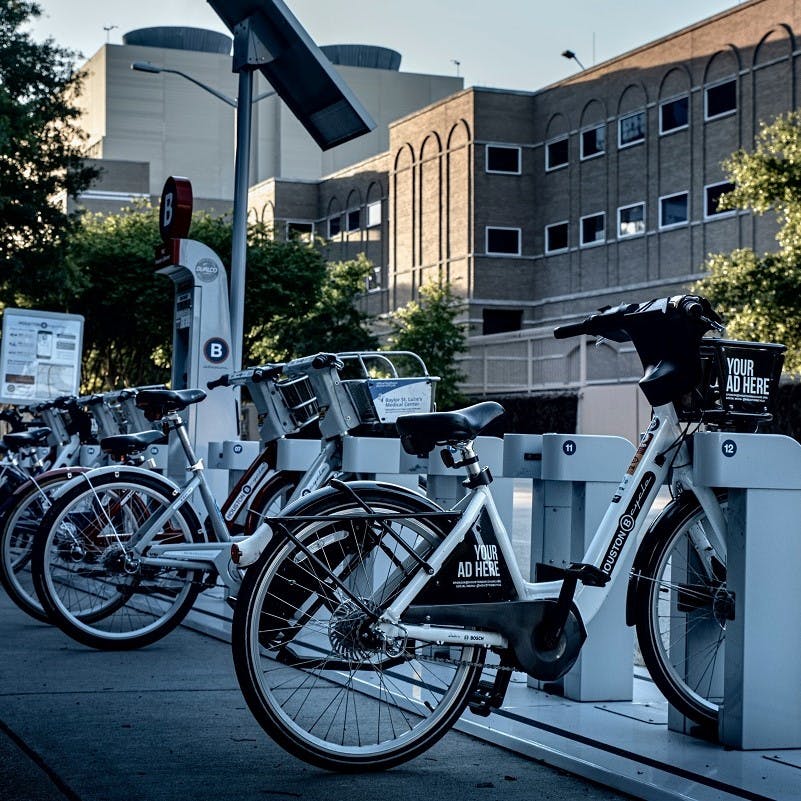 Electric bikes lined up at a charging station outside an office building where employees choose cycle-to-work schemes as perks.
