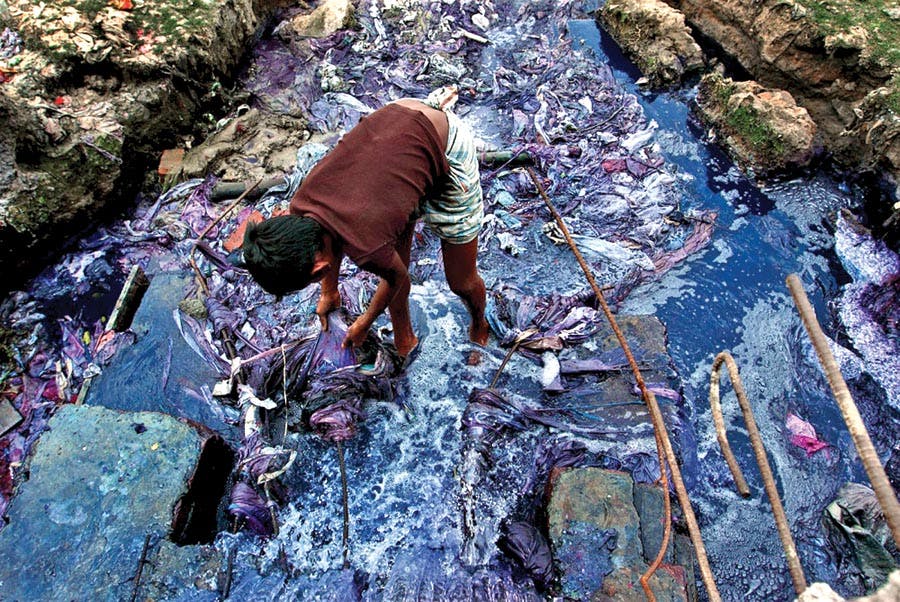 A boy standing in a polluted river caused by the production of fast fashion. Sustainable fashion doe not create such environmental problems.