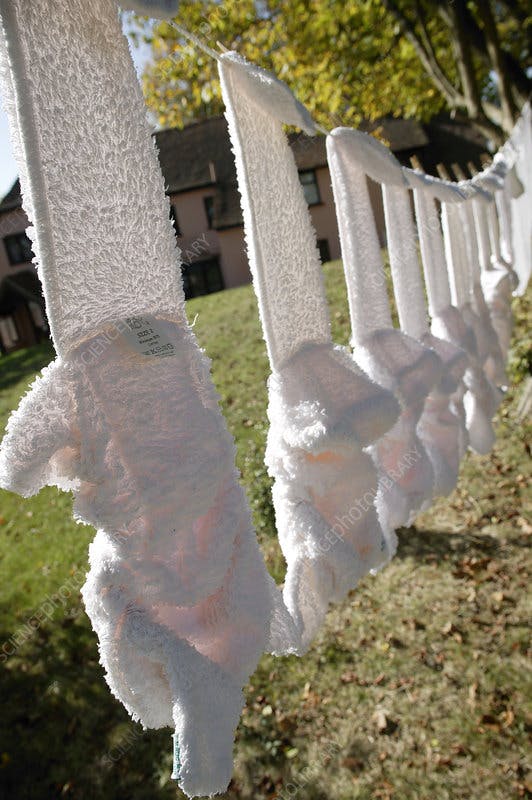 Ten white reusable nappies hanging out to dry on a washing line. 