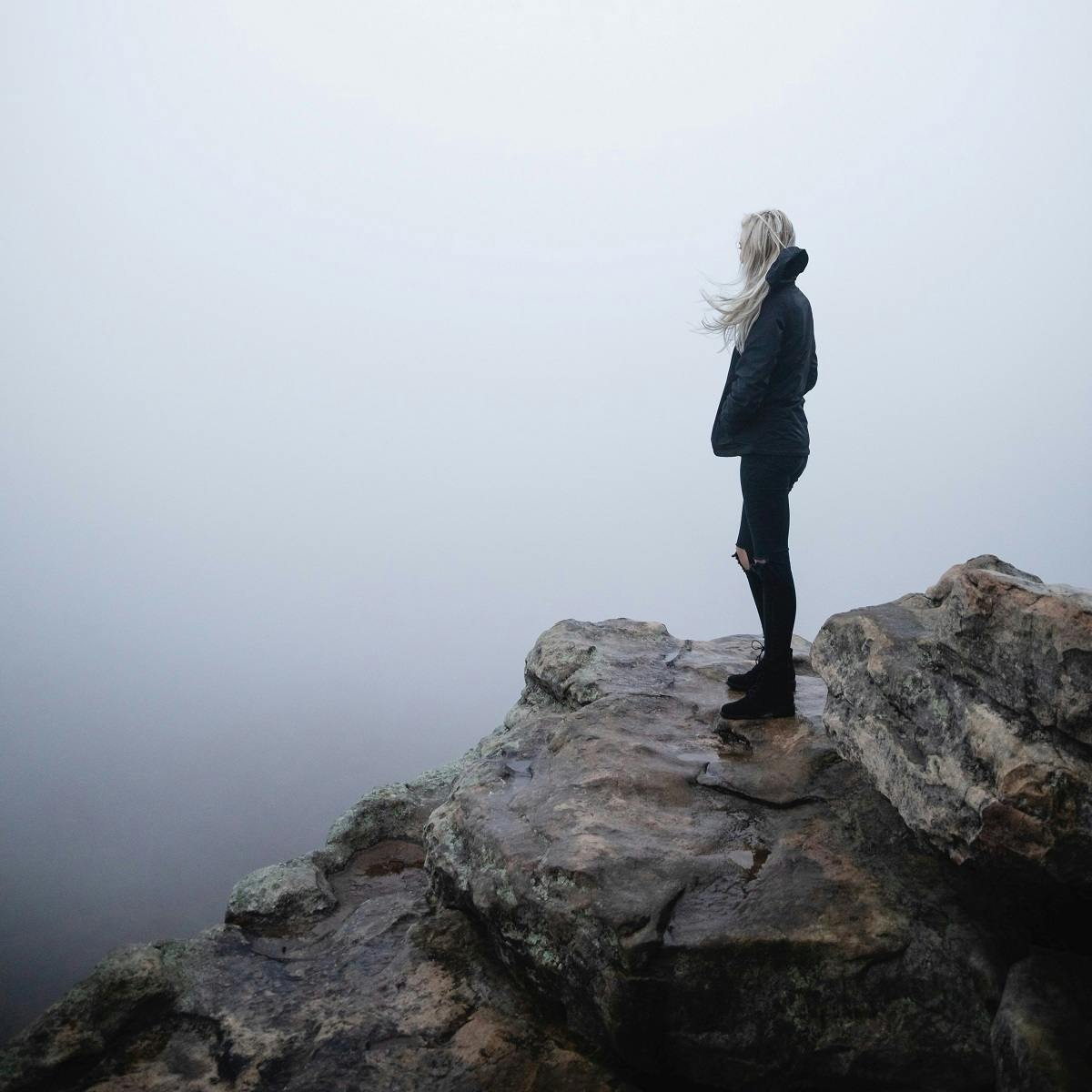 An anxious looking woman looks out over the mist from a rocky outcrop. Anxiety is on the increase in our modern world, in particular, eco anxiety.