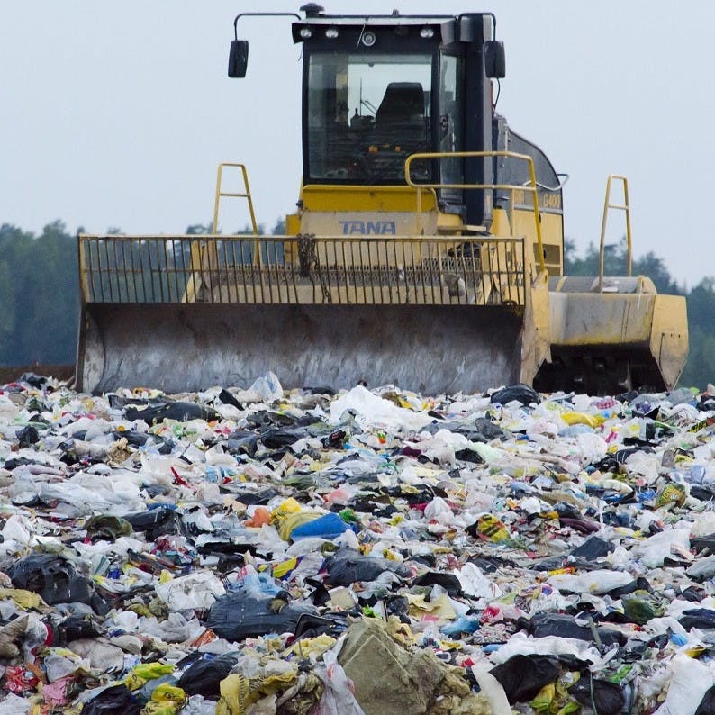 A bulldozer surrounded by waste at al landfill site adjacent to a beautiful forest. Disposable nappies make up for a significant amount of landfill waste.