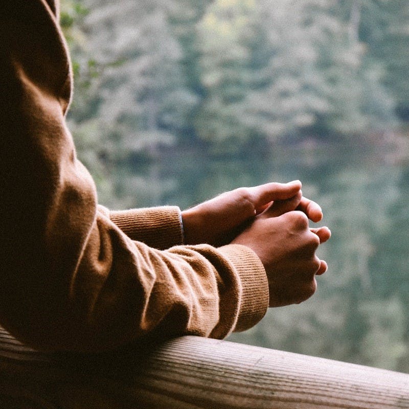 A person pausing for thought on a bridge overlooking a lake and trees. Taking time out each day to pause and collect your thoughts, even if 5 minutes, is step closer to Slow Living. 