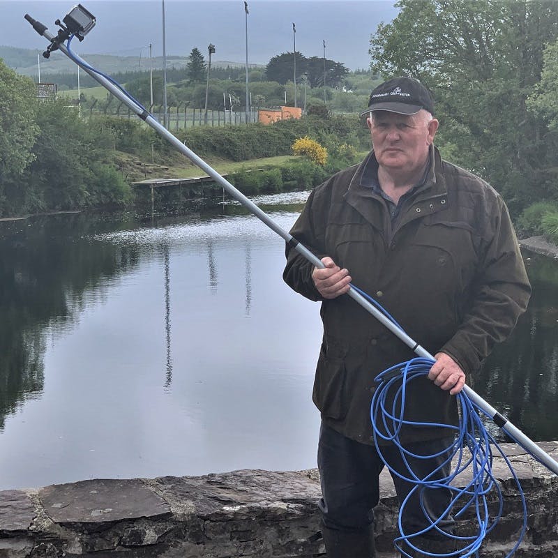 John Murphy from Salmon Watch Ireland holding a camera with an extension pole and blue cables. 