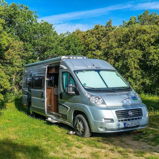 A modern Fiat Ducato camper van parked in a forest