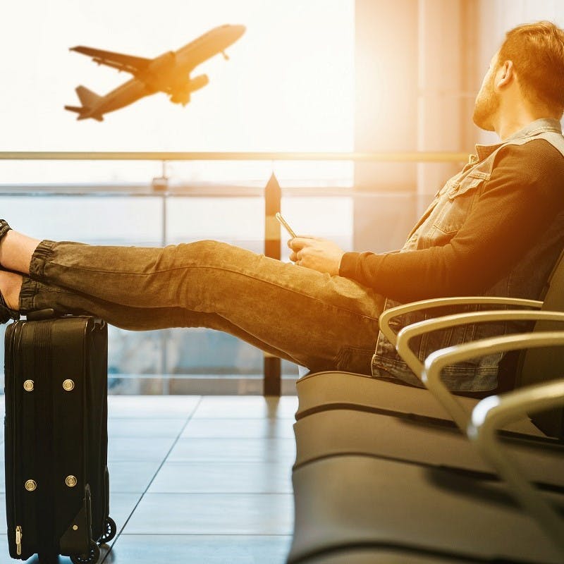 A man waiting in the departures lounge at an airport. An easy tip to sustainable flying is to pack light.  