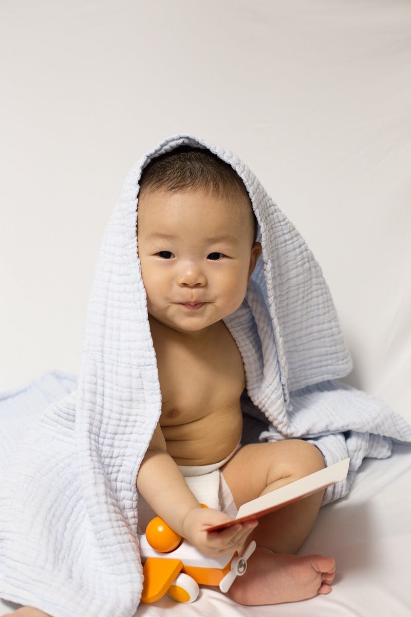 A young toddler playing with a toy aeroplane with a towel over his head