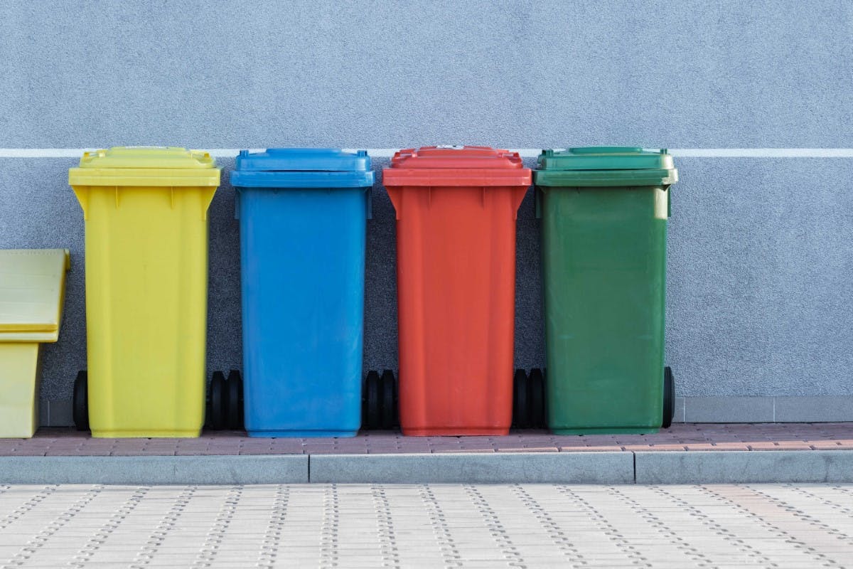 Four colorful recycling bins side by side on a sidewalk.