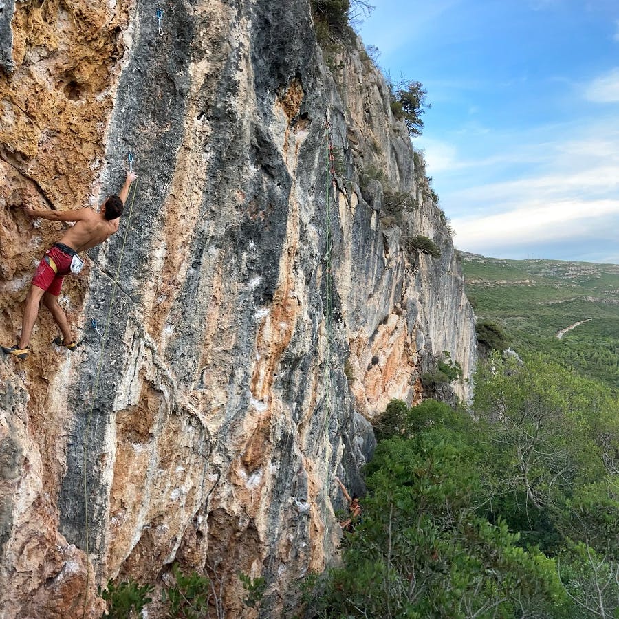 A sport climber ascending a steep rock face with the beach on the background