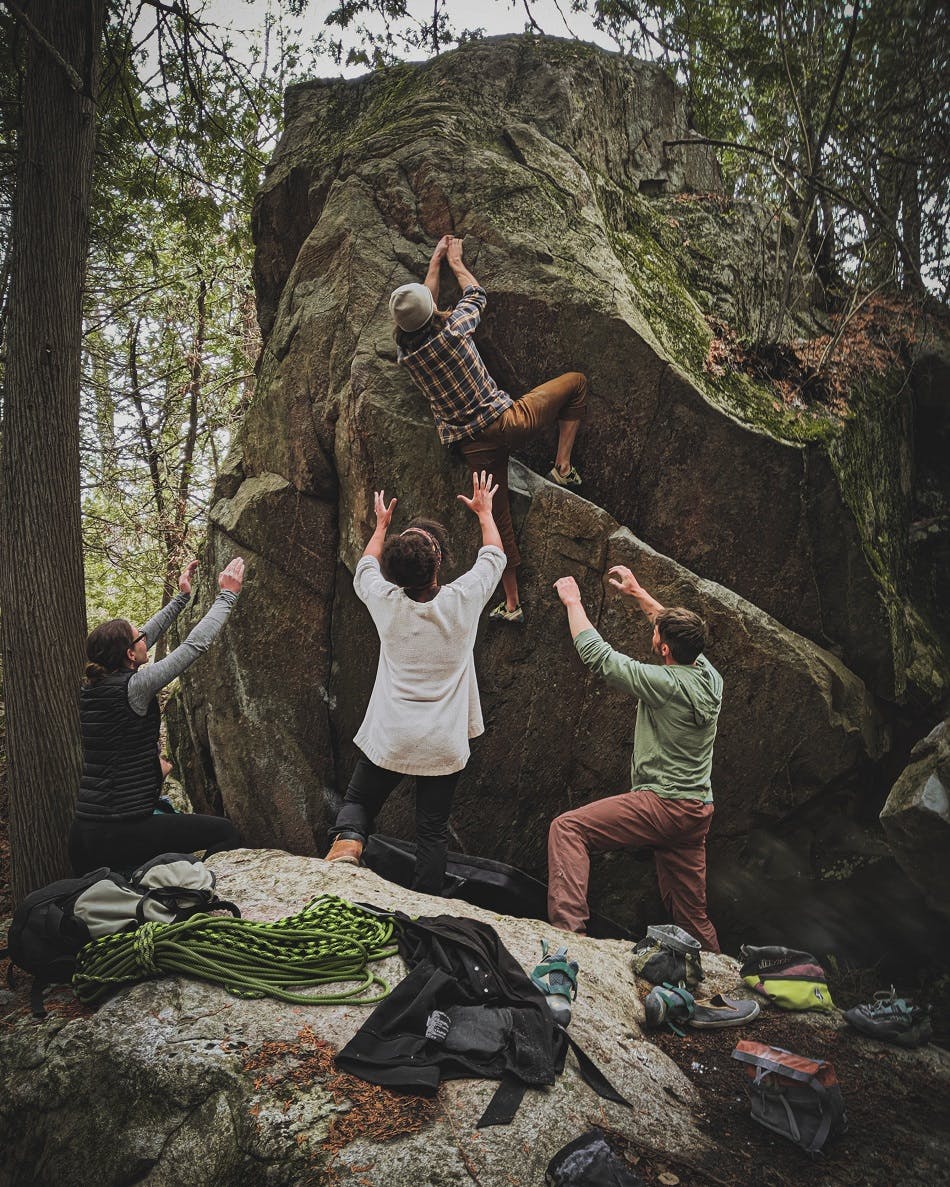 A group of climbers help a novice climber up a boulder.