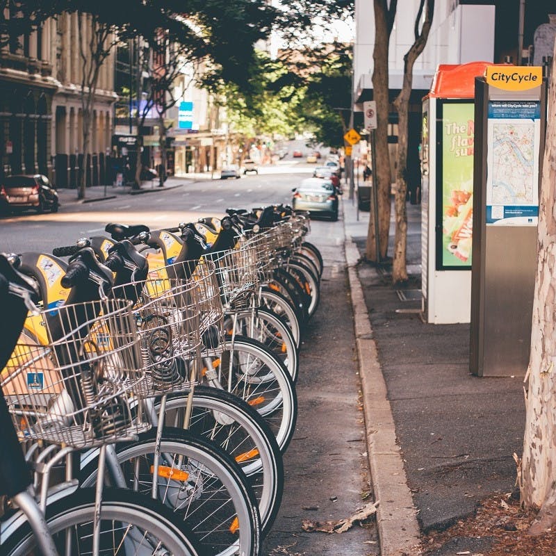 A row of e-bikes lined up along a city's sidewalk. With all modern cities offering e-bikes, the idea of a green commute is that much more realistic. 