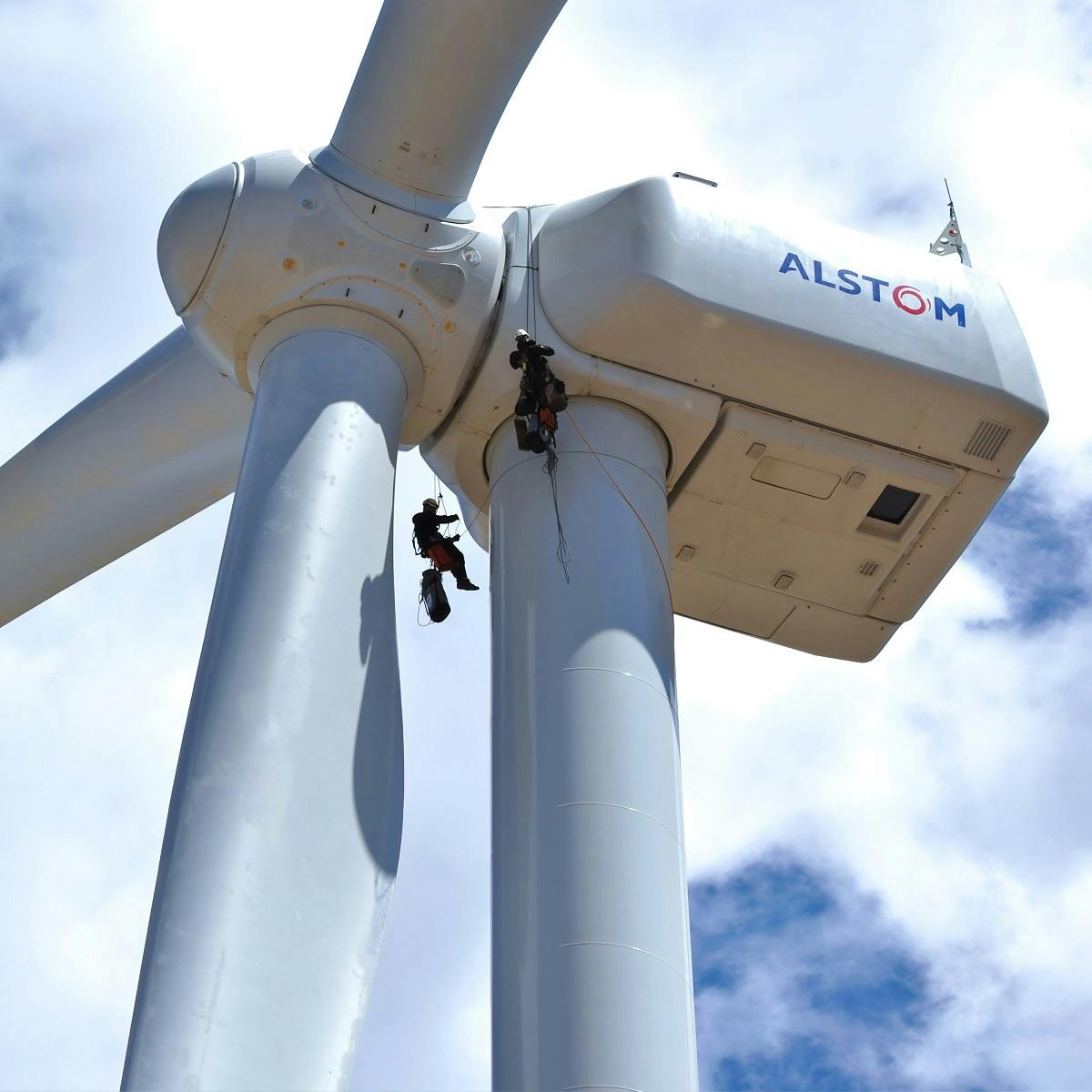 Two men on ropes maintaining a wind turbine