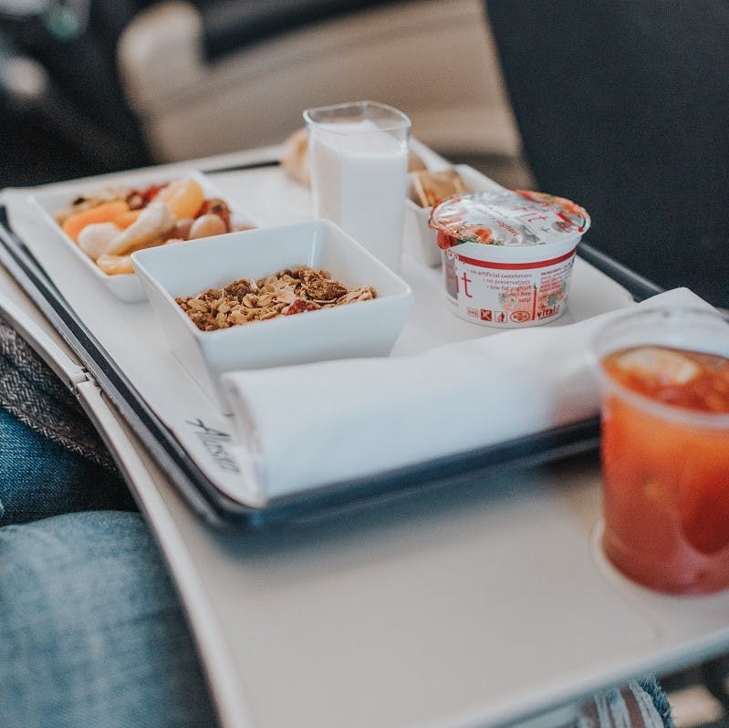 A person eating breakfast on a plane, which consists of muesli, yoghurt, fresh fruit and juice. Request a vegan meal next time you fly to ensure more sustainable flying. 
