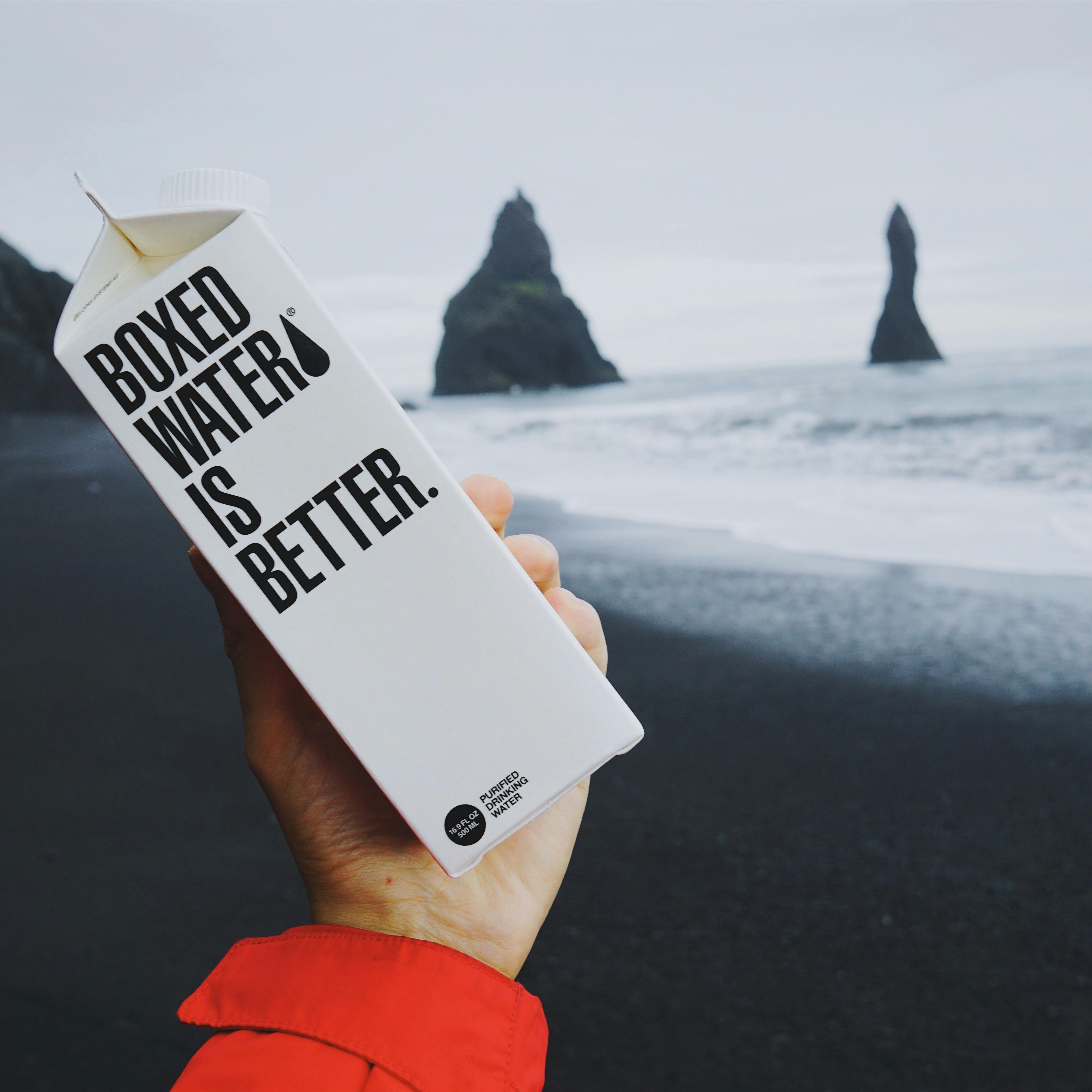 A person holding boxed water on a beach. 