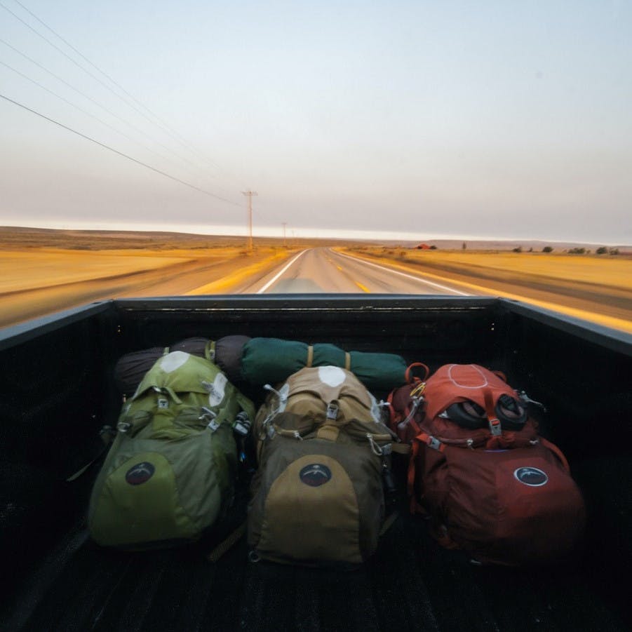 Three backpacks and camping gear in the back of a pick up. Hitchhiking is an adventurous way to travel without flying