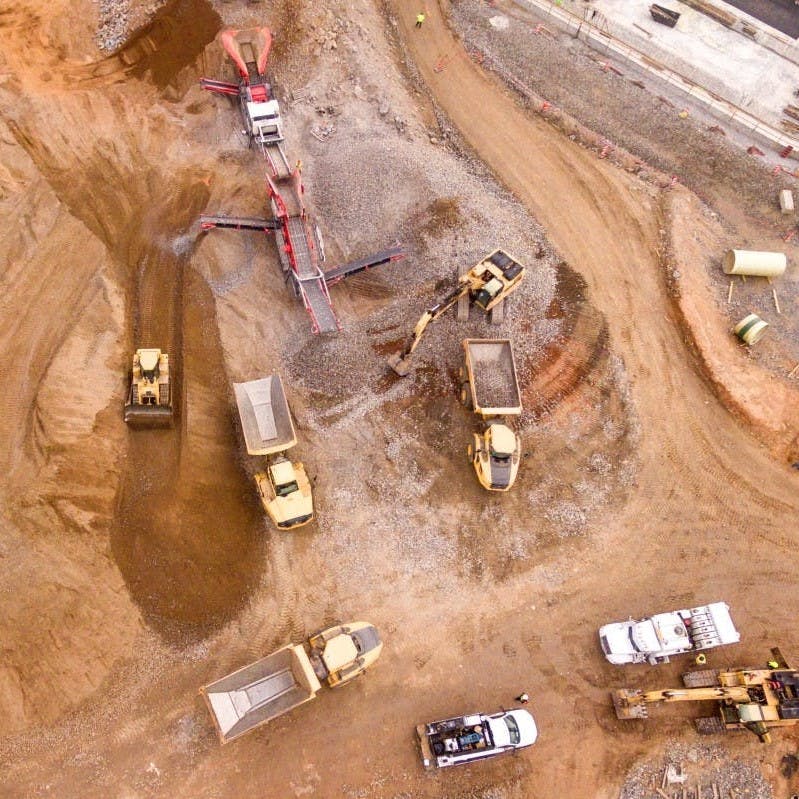Mining site shown from above, showing machinery and vehicles over brown sandy soil. 