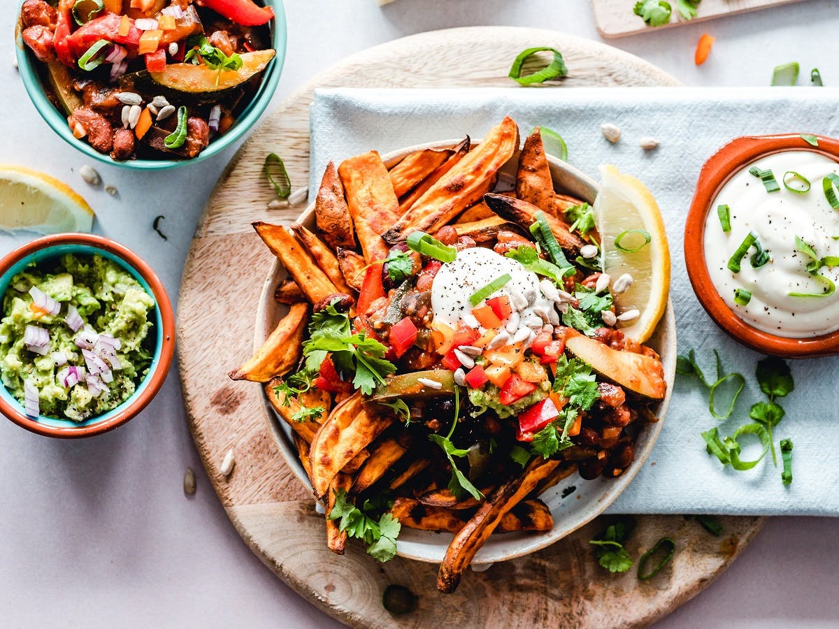 Going vegan means getting creative! A plate of sweet potato chips topped with vegan sour cream and accompanied with a side dish of guacamole