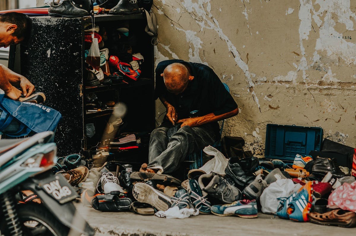 A repairing shoes on the street. Keeping your shoes and clothes in circulation longer will help you reduce your carbon footprint.  