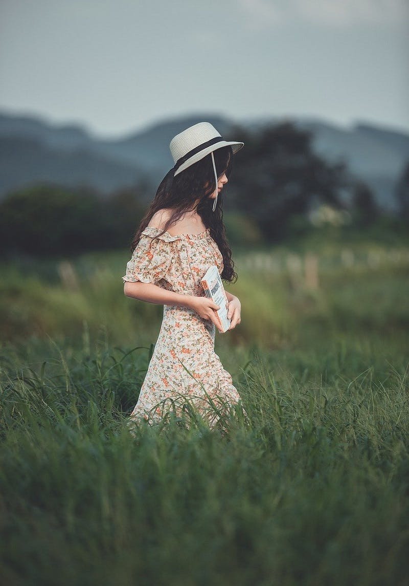 A woman wearing a summer dress strolls through a field.