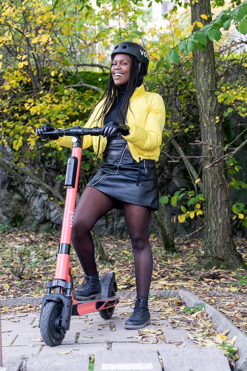 A woman commuting to work on an electric scooter wearing a helmet.