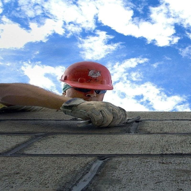 A brick layer builds a wall with the sky above him. Building an eco house eliminates the need for unsustainable materials like bricks and concrete.