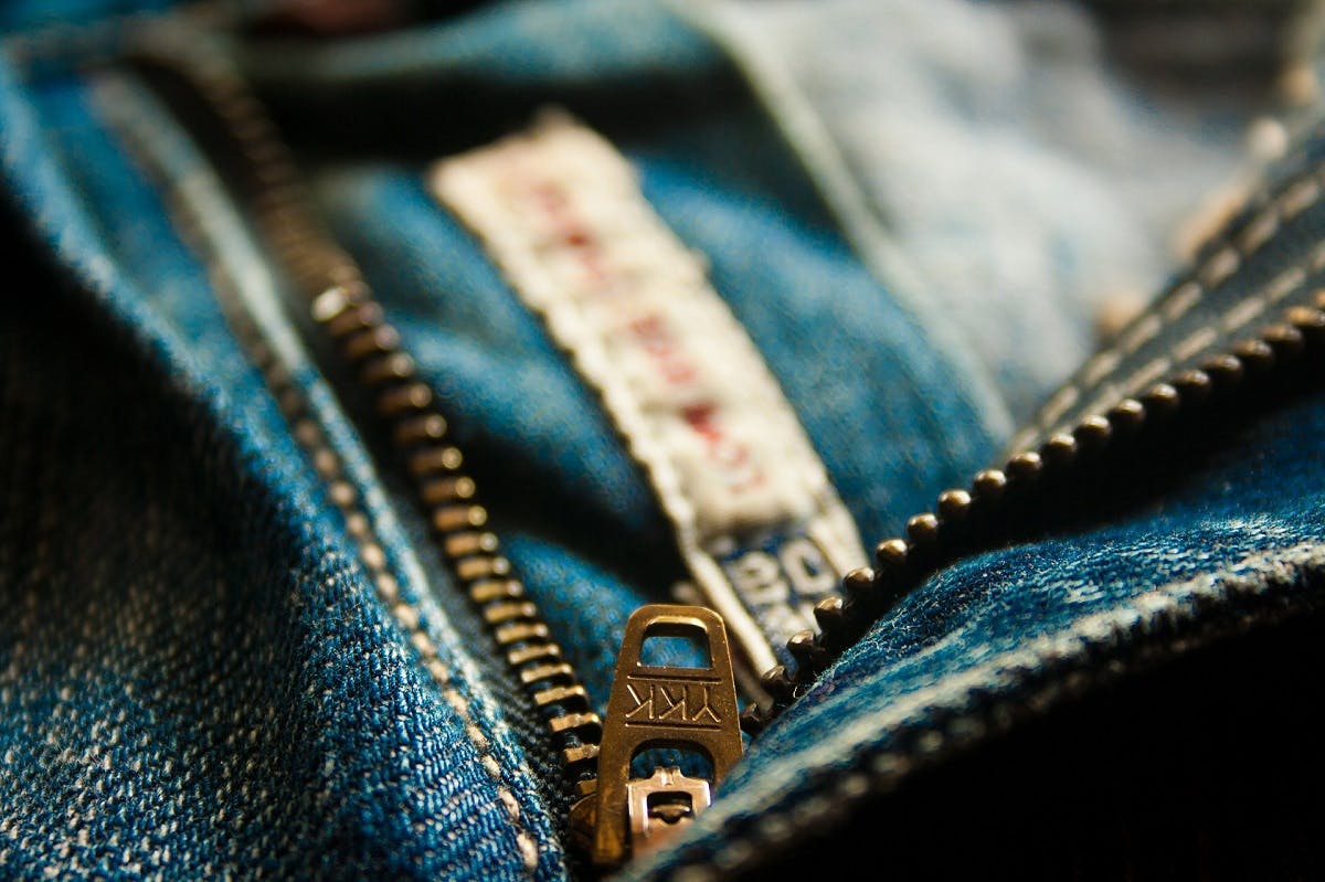 A close up photo of a YKK zip on a pair of blue jeans. Look for these signs of quality when trying to avoid fast fashion.
