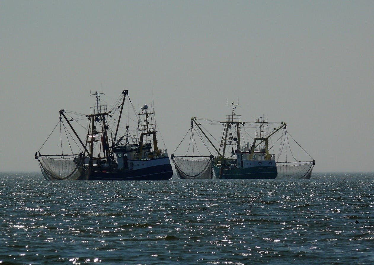 Two fishing trawlers casting their large drag nets out on the high seas