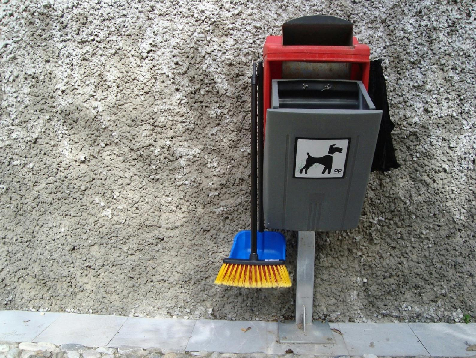 A dog poo bin complete with bags, a dust pan and brush.