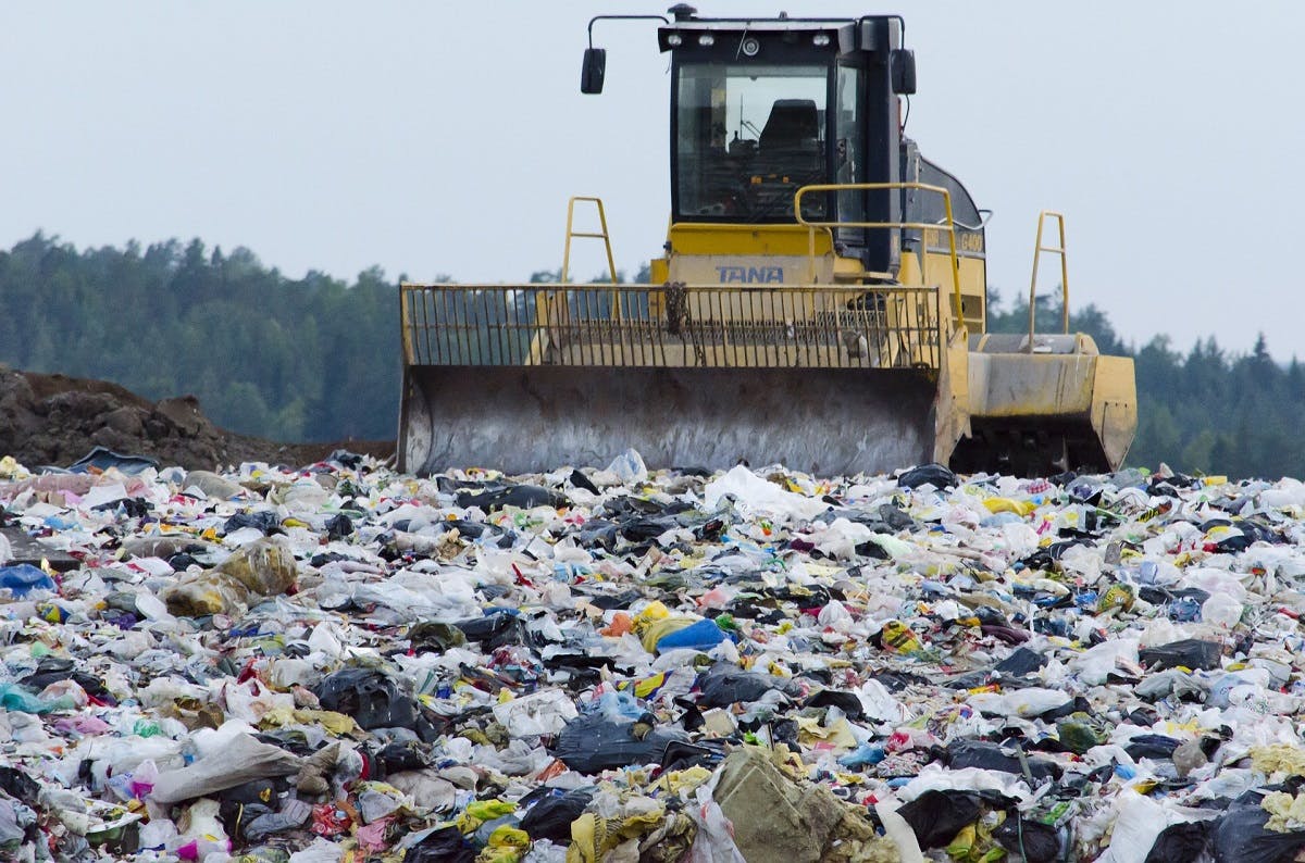 A bulldozer surrounded by waste at al landfill site adjacent to a beautiful forest